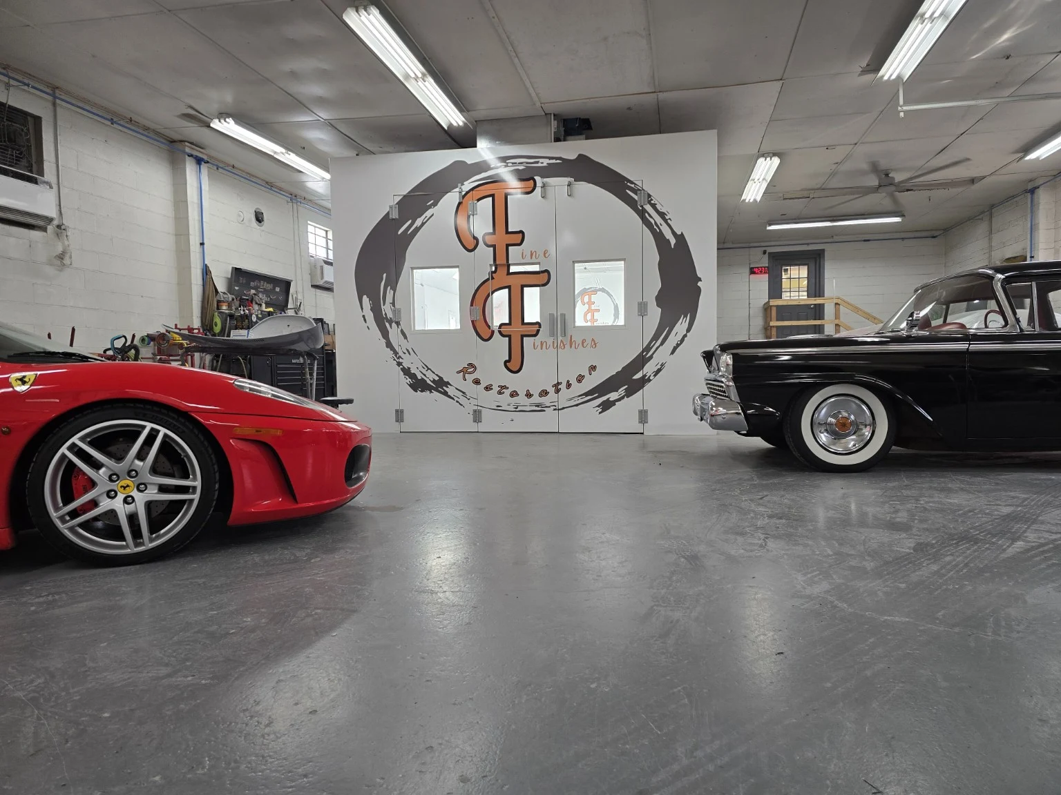 Red Ferrari and black 1959 Ford in front of the Fine Finishes paint booth and logo