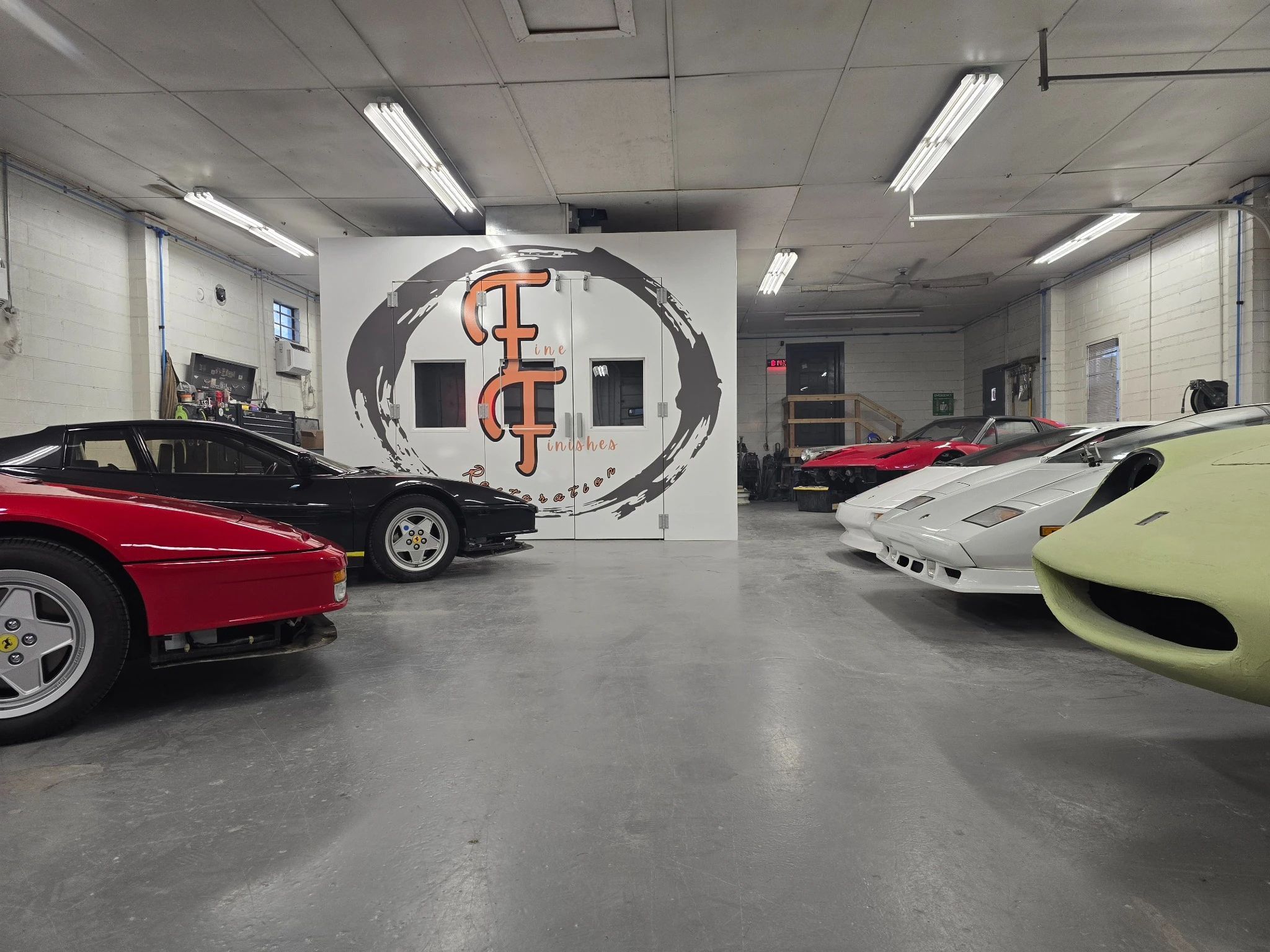 Classic Ferraris and Lamborghinis in the Fine Finishes workshop, with the orange and gray logo on the paint booth